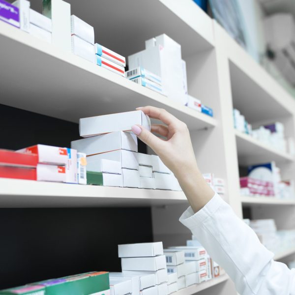 Closeup view of pharmacist hand taking medicine box from the shelf in drug store.